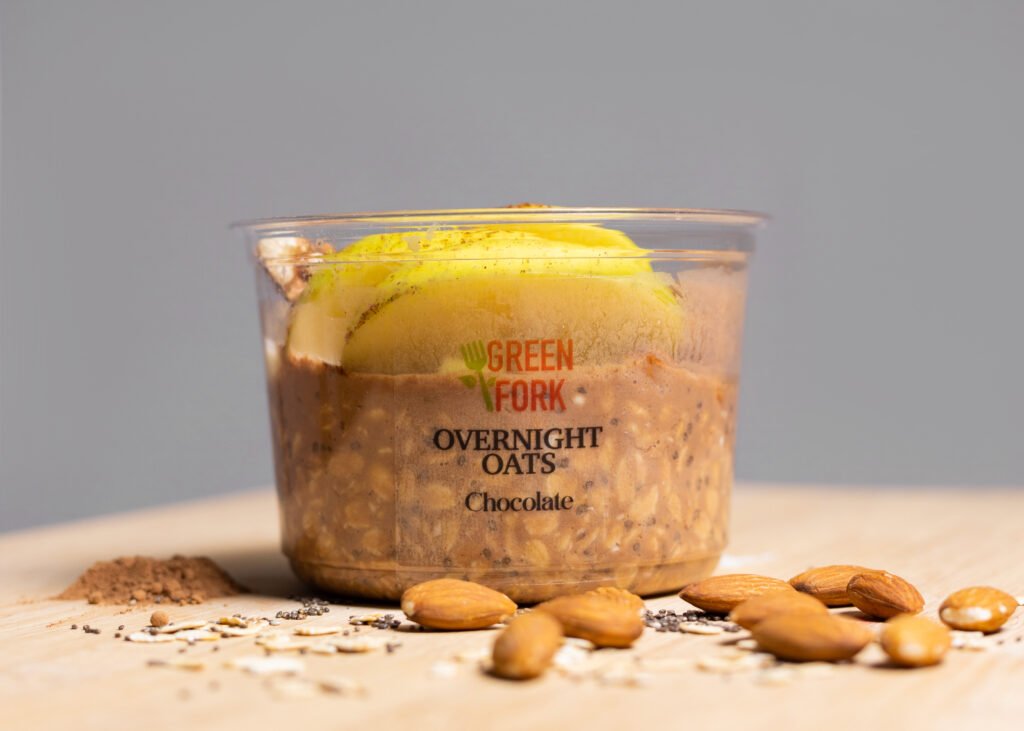 A Greenfork overnight oats cup topped with mango, with almonds beside it