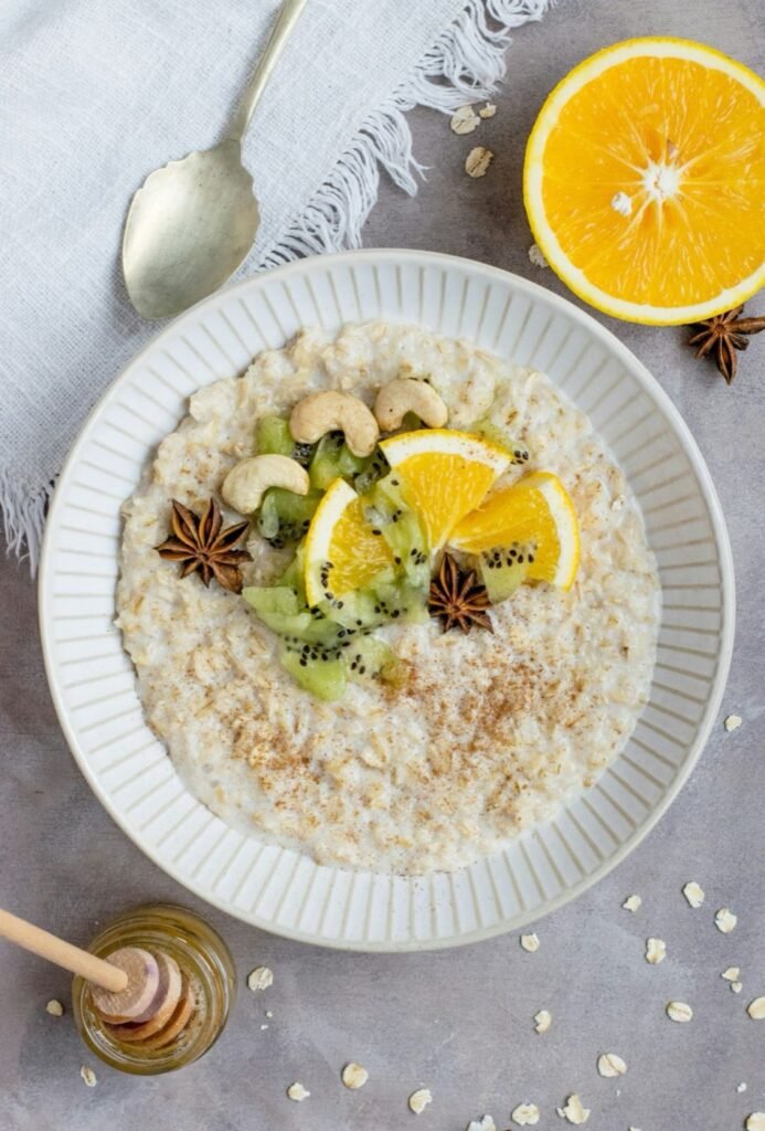 A bowl of creamy oats topped with orange, kiwi and cashews, with honey alongside