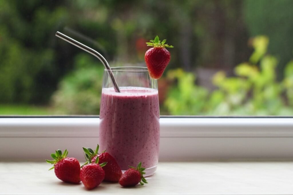 A strawberry smoothie in a glass on a windowsill with fresh strawberries beside it